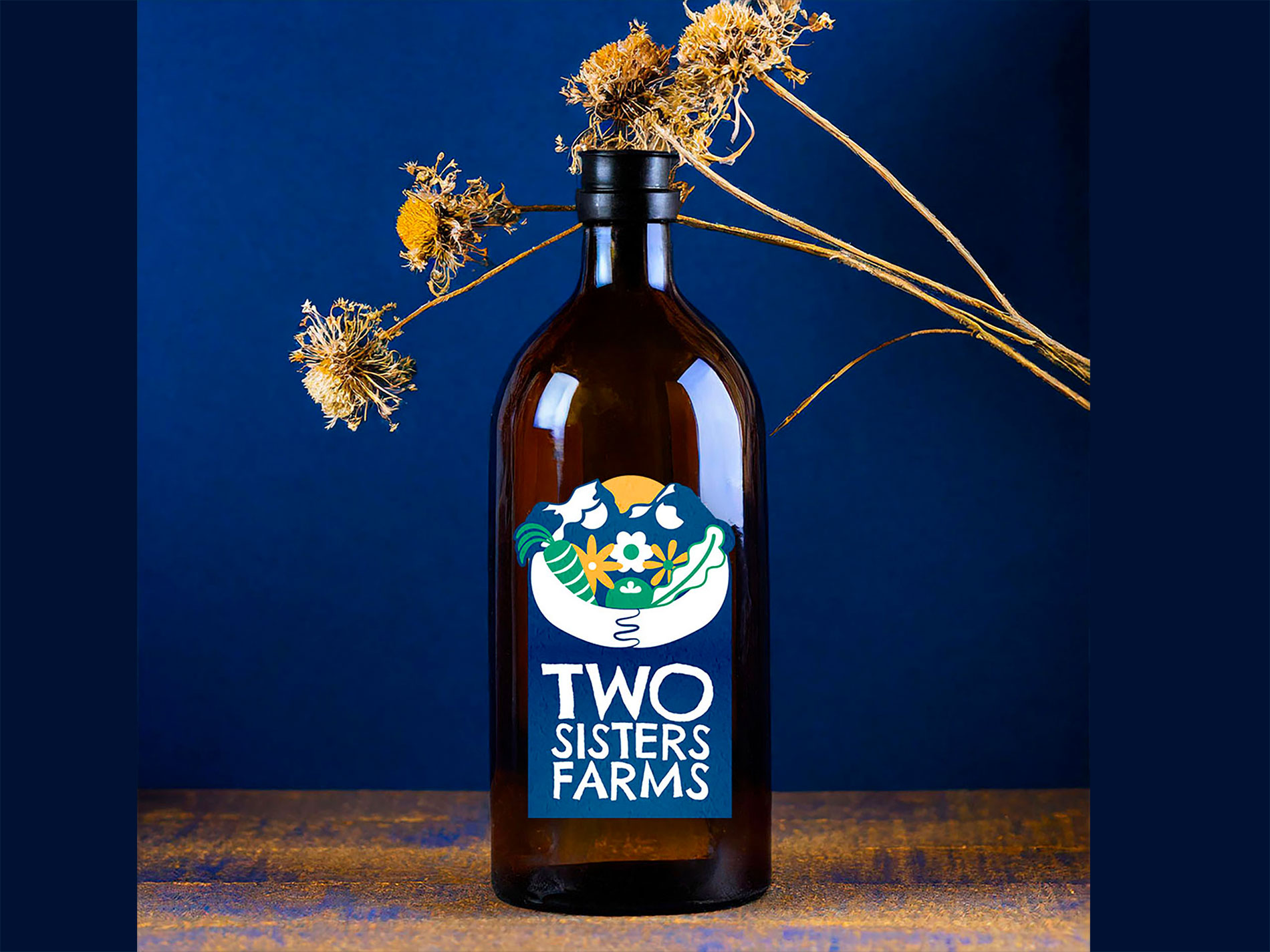 A dark glass bottle holding dried flowers in it has a two sisters farms logo in front with a deep blue background