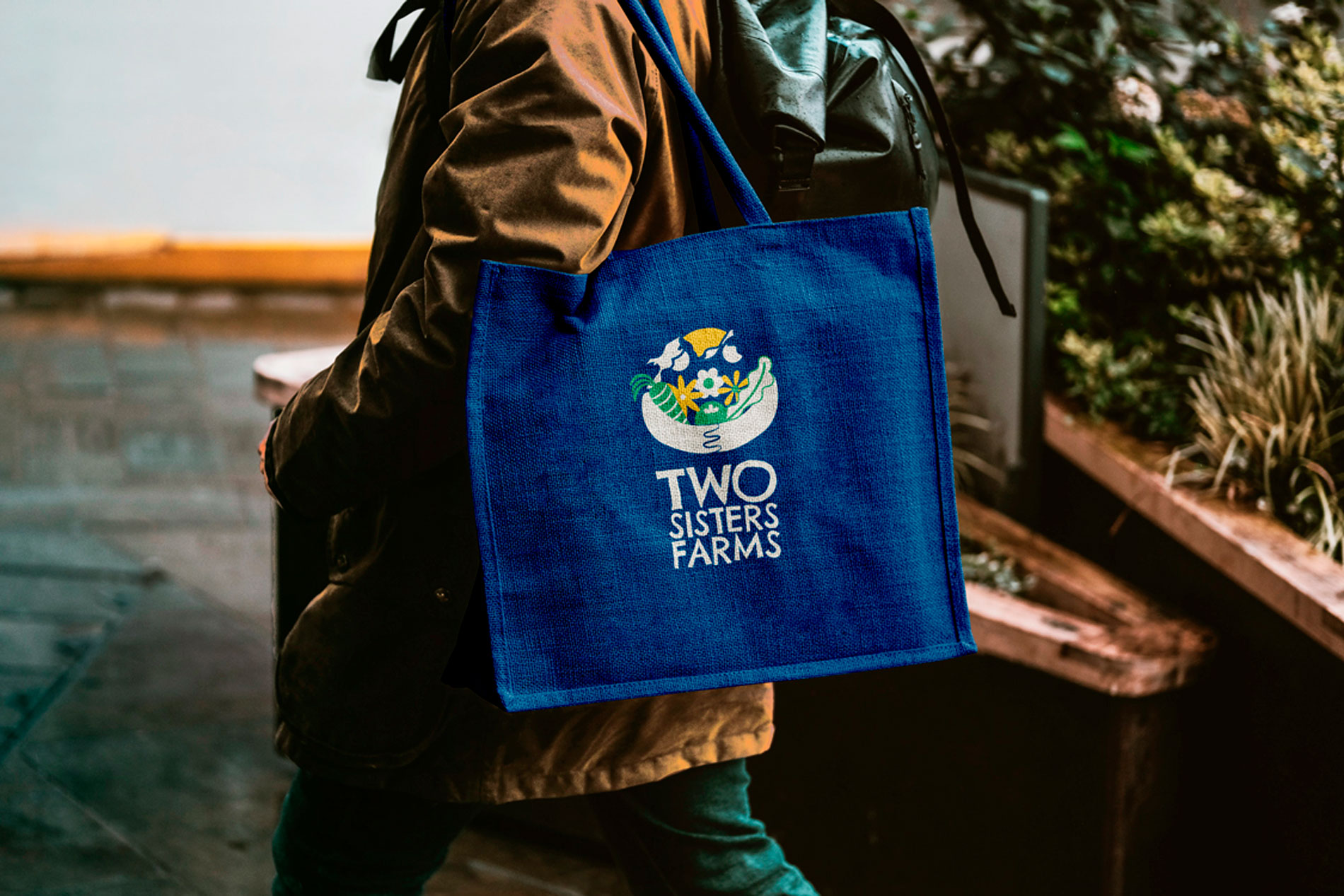 Person walking through the rain with a blue totebag that has the Two Sisters Farms logo on it