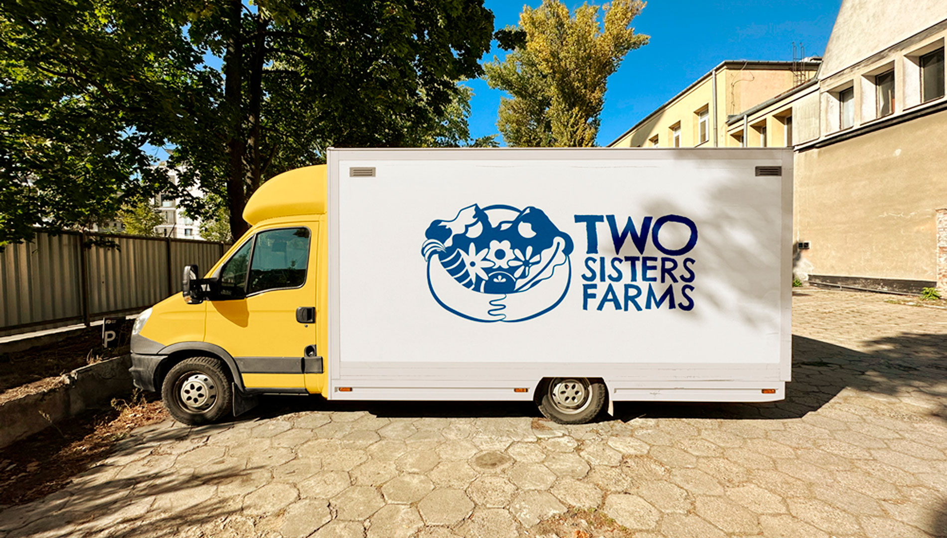 Industrial truck with yellow cab and white box, with a two sisters farms logo